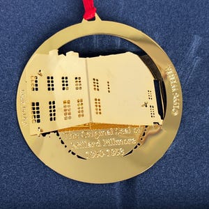 May include: A gold-colored Christmas ornament with a building silhouette and the text "The Original Seal of Millard Fillmore 1850-1853." The ornament is circular with a red ribbon for hanging.