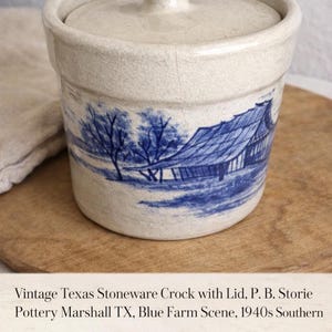 Puede incluir: Olla de gres vintage con tapa. La olla blanquecina presenta un diseño de escena de granja azul. La tapa tiene un asa de pomo. La olla está sobre una superficie de madera.