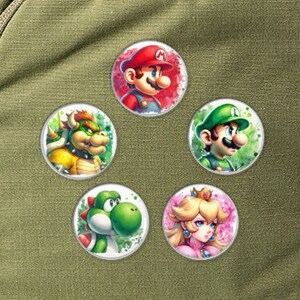 May include: Five round pins featuring characters from the Super Mario Bros. video game franchise. The pins are white with a colorful image of Mario, Luigi, Bowser, Peach, and Yoshi.