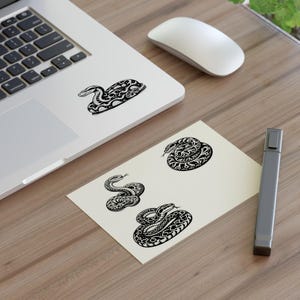 Può includere: Un set di quattro adesivi di serpente in bianco e nero. I serpenti sono in varie pose, tra cui arrotolati e striscianti. Gli adesivi sono perfetti per aggiungere un tocco di fantasia a laptop, borracce o diari.
