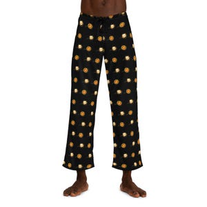 Op de afbeelding: Zwarte pyjamabroek met een all-over patroon van oranje en witte gebakken eieren in een koekenpan. De broek heeft een taille met trekkoord en een relaxte pasvorm. De pyjamabroek is gemaakt van een zacht, comfortabel materiaal.