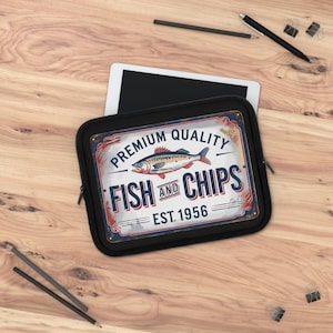 以下が含まれることがあります： ヴィンテージスタイルの「Fish and Chips」サインが付いた黒いタブレットスリーブ。サインには魚のイラストと「Premium Quality」と「Est. 1956」の文字が描かれています。スリーブは、鉛筆とペンが置かれた木製の表面にあります。