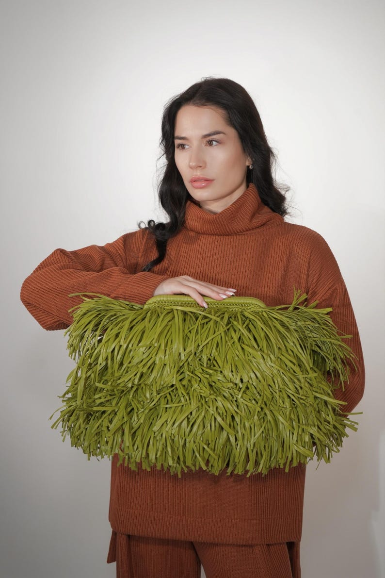May include: A rectangular clutch bag in a vibrant olive green color, featuring a dense exterior layer of long, thin, fringed strips. The bag has a structured, woven top frame and a secure clasp closure, providing a textured and layered appearance.