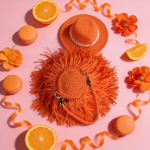 May include: A bright orange crochet handbag with long fringe detailing and a matching crochet hat with a white ribbon band. The set is surrounded by orange macarons, orange slices, and orange flowers on a solid light pink background.