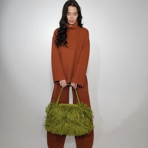 May include: A rust-colored ribbed knit sweater and matching wide-leg trousers paired with a lime green handbag covered in long, dense fringe. The handbag features two top handles and a structured frame, contrasting with the solid knit outfit.