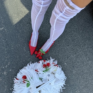 May include: White sheer thigh-high stockings with a vertical seam, red pointed-toe pumps featuring a green and red crocheted cherry embellishment, and a white fringed handbag decorated with multiple small red crocheted cherry accents.