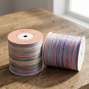 Può includere: Due rocchetti di nastro decorativo dai colori pastello, tra cui rosa, blu, verde e viola. Il nastro è fatto di sottili strisce a strati. Una bobina è in posizione verticale e l'altra è di lato. La parte superiore di una bobina dice "Ispie".