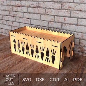 May include: A light-colored wooden storage box with carrot-shaped cutouts and a scalloped top edge. The box is rectangular and sits on a wooden surface. The words "LASER CUT FILES" and file type abbreviations are visible.