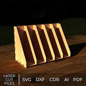 May include: A wooden organiser with five angled slots, suitable for storing documents or files. The light-coloured wood contrasts with the dark shadows within the slots. The text "LASER CUT FILES" and file type abbreviations are visible.