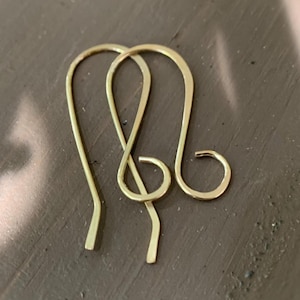 Peut inclure: Deux crochets de boucles d'oreilles dorés, présentés sur une surface marron. Les crochets sont faits de fil métallique fin et courbé, avec un design en boucle. Les crochets sont conçus pour être portés dans les oreilles percées.