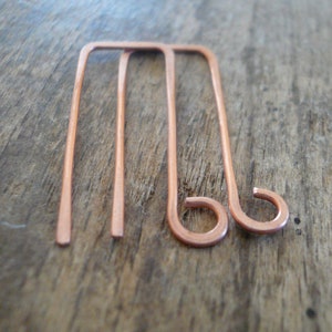 May include: A pair of copper wire earrings with a simple rectangular shape and a curved hook closure.