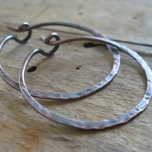 May include: A pair of hammered copper hoop earrings with a wire closure. The earrings are a dark copper color with a hammered texture.