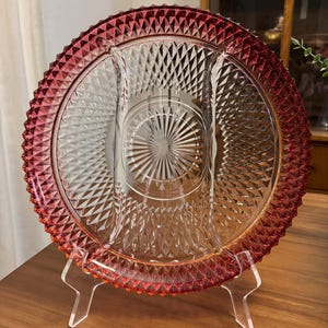 May include: A vintage glass serving dish with three divided sections. The dish has a clear glass center with a diamond pattern and a red rim with a gradient effect.