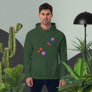 Könnte beinhalten: Ein dunkelgrüner Kapuzenpullover mit dem Text "Just Live!" in Blau und roten Blumen, die auf der Vorderseite gestickt sind.