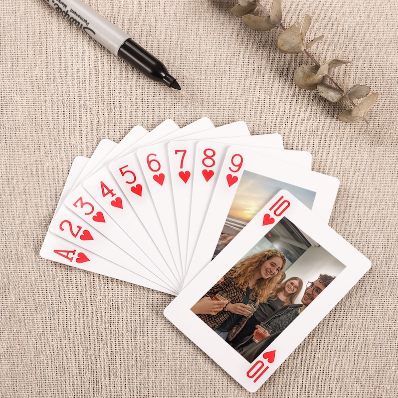 May include: A set of playing cards with a photo of three people on the 10 of hearts card. The cards are fanned out and the 10 of hearts is on top.