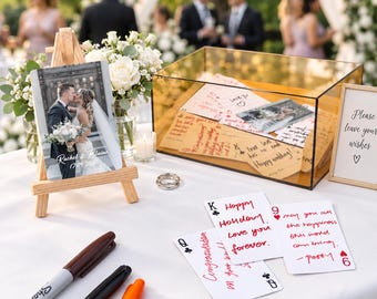 Puede incluir: Un set de libro de firmas para bodas con una caja de acrílico ámbar transparente llena de tarjetas escritas a mano, un pequeño caballete de madera con una foto de pareja y el texto Rachel & Blaine 17.09.2020, tres rotuladores y un cartel Please leave your wishes.