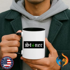 May include: White ceramic mug with a black interior and handle. The mug features the word "Stoner" in a gothic font with a green cannabis leaf replacing the "o" on a black rectangular background.