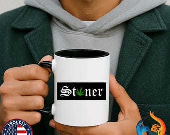 May include: White ceramic mug with a black interior and handle. The mug features the word "Stoner" in a gothic font with a green cannabis leaf replacing the "o" on a black rectangular background.