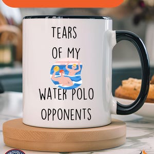 May include: White ceramic coffee mug with a black rim and handle. The mug features a graphic of two people playing water polo with the text "Tears of my Water Polo Opponents".