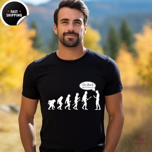 以下が含まれることがあります： 人間進化の白いグラフィックがプリントされた黒いTシャツ。グラフィックは、サルから現代人へと進化する棒人間の列を示しています。列の最後の図形は、サルを指さし、「Go Back We F*cked Up」と書かれた吹き出しがあります。
