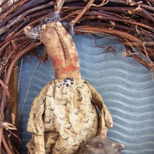 May include: A handmade rag doll with brown fabric and a floral print dress. The doll is holding a brown fabric animal in its arms. The doll is sitting on a white crocheted surface.