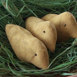 May include: Three brown felt birds with black eyes are nestled in a bed of green grass.