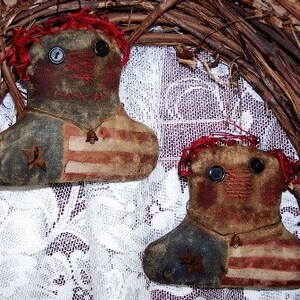 May include: Two handmade rag dolls dressed in red, white, and blue fabric with a star and stripes pattern. The dolls are decorated with small bells and have black button eyes.
