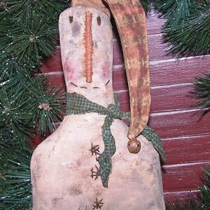May include: A handmade fabric snowman ornament with a brown and white striped hat, a green scarf, and a small bell. The snowman is made of white fabric and has a stitched-on face with a twig nose.