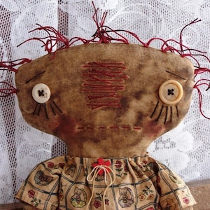 May include: A handmade rag doll with a brown face, red yarn hair, and two white buttons for eyes. The doll is wearing a brown and white dress with a floral pattern.