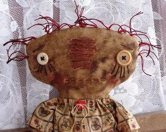 May include: A handmade rag doll with a brown face, red yarn hair, and two white buttons for eyes. The doll is wearing a brown and white dress with a floral pattern.