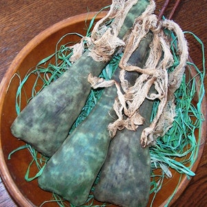May include: Three green and brown fabric gourds with white gauze wrapped around them. The gourds are sitting in a brown wooden bowl filled with green grass.