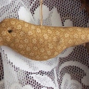May include: A beige bird-shaped pincushion with a floral pattern. The pincushion is made of fabric and has a slightly curved shape.