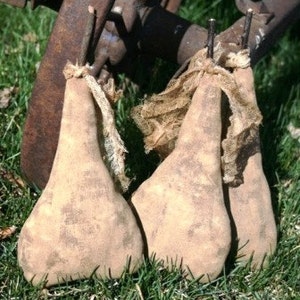 May include: Three brown fabric pears with a rustic, distressed look. The pears are tied with twine and have a burlap-like texture.