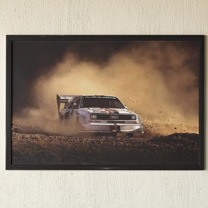 May include: A framed photograph of a white Audi rally car driving through a cloud of dust on a dirt track. The car is in focus, and the dust is blurred in the background.