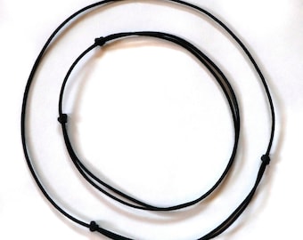 May include: A black adjustable cord necklace with two loops. The cord is made of a soft, flexible material.
