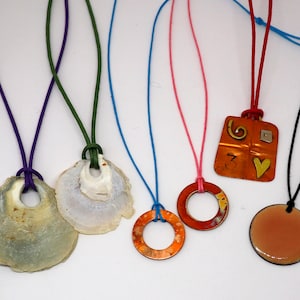 May include: Five necklaces with different pendants. The pendants include a seashell, a copper ring, a copper square with a heart and a number 3, a copper ring with a brown patina, and a round copper disc with a brown patina.