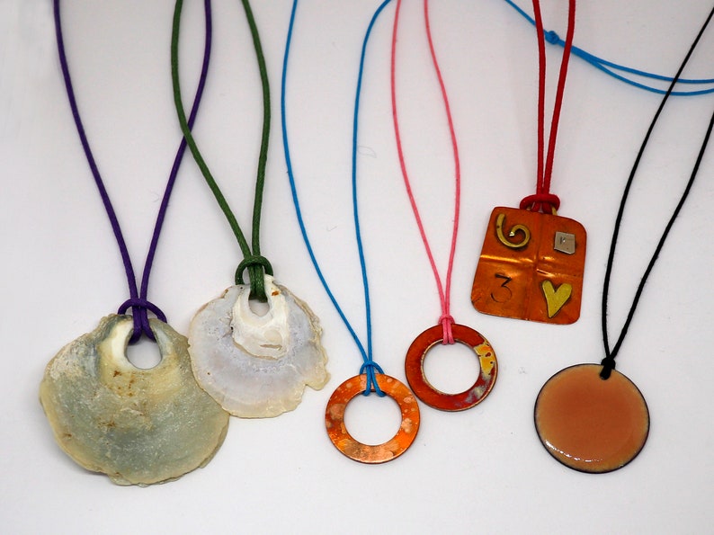 May include: Five necklaces with different pendants. The pendants include a seashell, a copper ring, a copper square with a heart and a number 3, a copper ring with a brown patina, and a round copper disc with a brown patina.