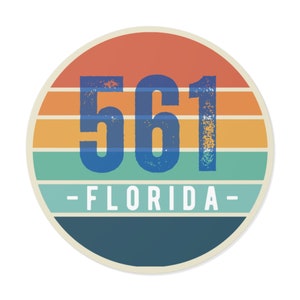 Könnte beinhalten: Ein runder Aufkleber mit einem Sonnenuntergangsdesign in Orange-, Gelb-, Grün- und Blautönen. Die Zahl 561 ist in Blau mit einem Used-Look gedruckt. Der Text -FLORIDA- ist in Weiß unter der Zahl gedruckt.