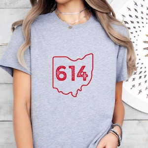 May include: Gray t-shirt with a red outline of the state of Ohio and the number 614 inside.