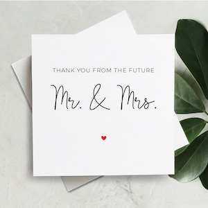 May include: White card with black text that reads "Thank you from the future Mr. & Mrs." with a small red heart below the text.