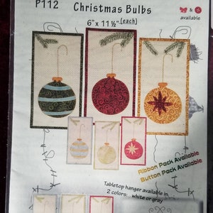May include: A craft pattern for making three Christmas bulb ornaments. The pattern includes instructions for making a striped bulb, a red bulb with swirls, and a gold bulb with a star. The pattern is 6 inches by 11 1/2 inches and is available in white or gray.