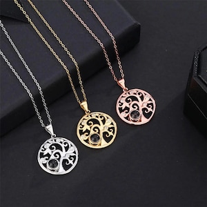 May include: Three necklaces with circular pendants. The pendants feature a tree of life design with a black center stone and small clear stones. The necklaces are silver, gold, and rose gold in color, each with a matching chain.