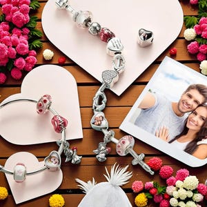 May include: A collection of silver charm bracelets with heart-shaped and floral beads. The bracelets are displayed on a wooden surface with pink heart-shaped cutouts, flowers, and a photo of a couple.
