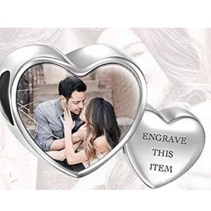 May include: A silver heart-shaped charm with a photo of a couple kissing inside. A smaller heart on the right side has the text "ENGRAVE THIS ITEM". The charm is designed to hold a personalized photo.
