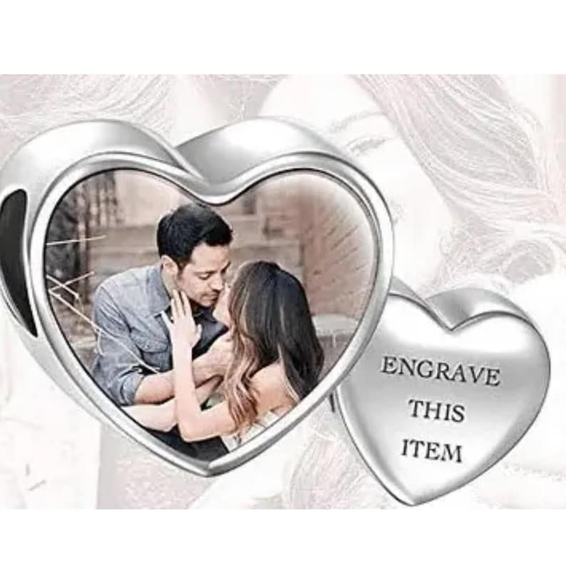 May include: A silver heart-shaped charm with a photo of a couple kissing inside. A smaller heart on the right side has the text "ENGRAVE THIS ITEM". The charm is designed to hold a personalized photo.