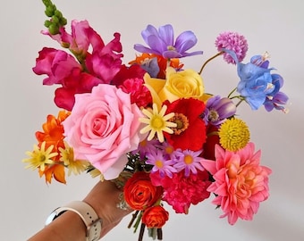 May include: A vibrant bouquet of flowers in shades of pink, yellow, blue, and red. The bouquet includes roses, carnations, and other blooms.