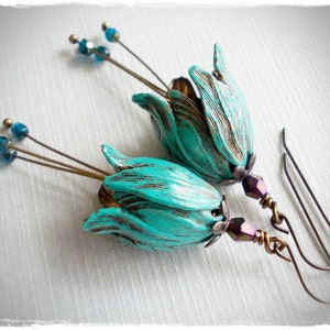 May include: A pair of turquoise blue flower earrings with a distressed finish. The earrings have a long, thin wire with small blue beads and a hook closure.