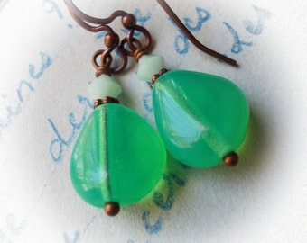 May include: A pair of green teardrop-shaped earrings with copper wire and beads. The earrings are hanging from copper hooks.