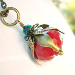 Op de afbeelding: Een ketting met een rode edelsteen hanger in een messing setting en een turquoise kraal. De hanger is gevormd als een bloem met bladeren.