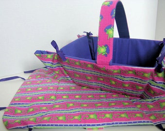 Könnte beinhalten: Ein rosa-lilafarbener Stoffkorb mit Frosch-Motiv und lilafarbener Innenausstattung. Der Korb hat einen Griff und ist aufgeklappt, um das Innere zu zeigen.